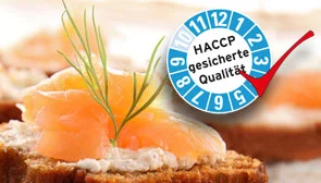 Ein belegtes Brötchen, daneben eine HACCP-Plakette mit der Aufschrift 'HACCP gesicherte Qualität'